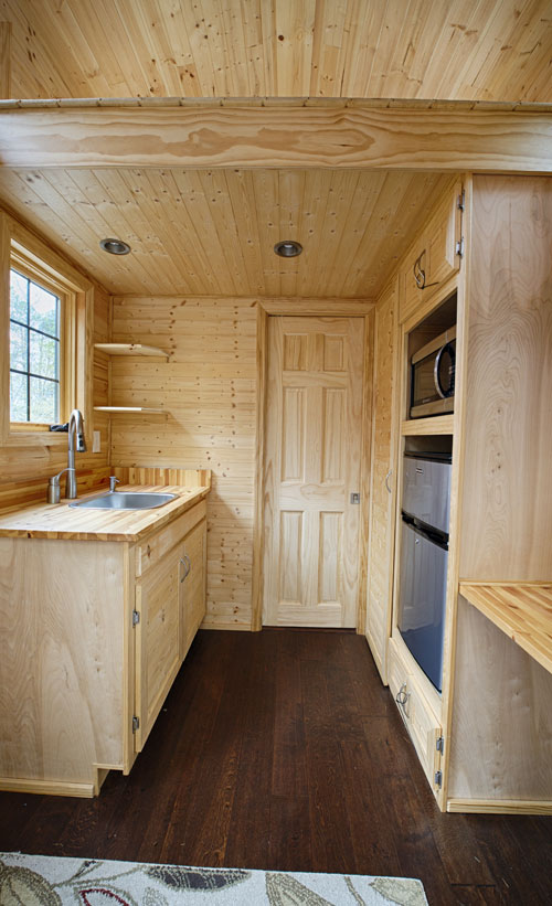 This natural wood tiny house kitchen features a galley design. Simple and functional, this tiny house kitchen layout is worth considering.