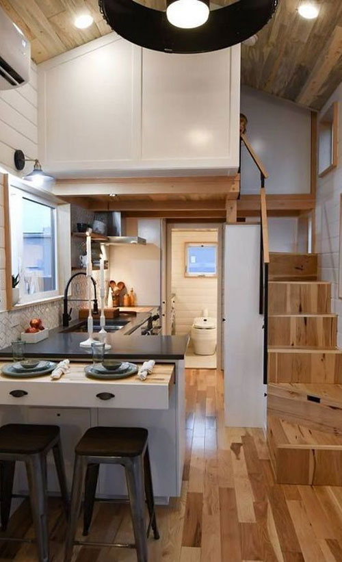 High ceilings and a pullout eating space make this tiny house kitchen design functional and roomy.