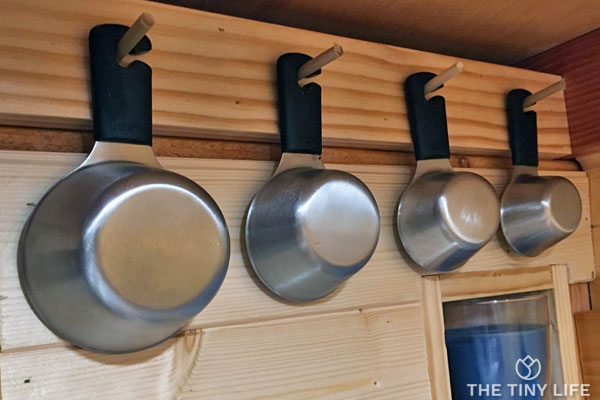 Measuring cups are hung on wooden hooks out of the way but within easy reach in this tiny house kitchen.