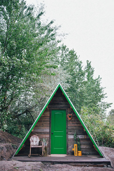 This A-frame tiny house has a bright green door and horizontal wooden siding for rustic appeal.