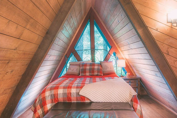 The loft of this A-frame tiny house features plenty of room for a standard double bed and nightstand.