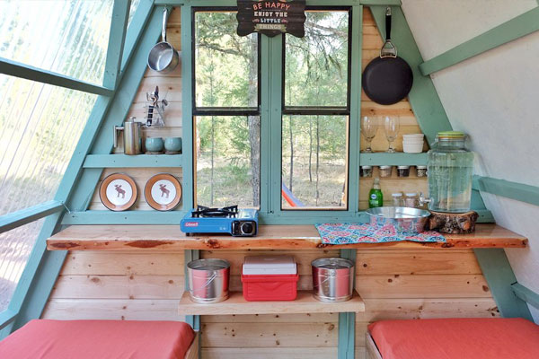 The interior of this A-frame tiny cabin is perfect for camping with a small kitchenette and two sleeping areas.